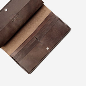 a dark brown leather wallet lying open on a flat surface. The wallet has multiple internal pockets, hand stitching and metal hardware closures.