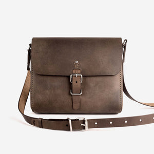 A dark brown leather satchel with hand stitching, stainless steel hardware closures, shoulder strap and etched logo detailing