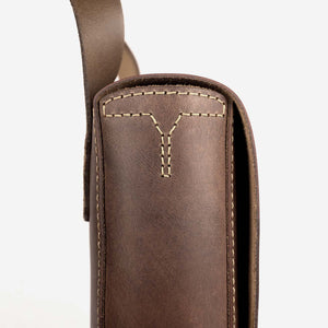 side view of a a rich brown leather satchel with shoulder strap and hand stitched detailing.