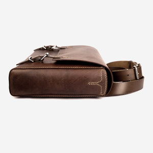 side view of a a rich brown leather satchel with shoulder strap, stainless steel hardware and hand stitched detailing.
