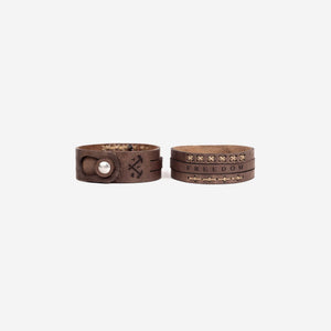 two dark brown leather wristbands in a front and back profile format. Both with logo, font and stitching details