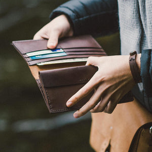 a person holding a dark brown leather wallet, open wide to reveal contents of multiple bank card pockets.