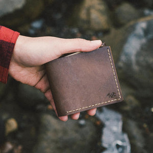 a hand holding a rich brown leather wallet with and etched logo and hand stitched detailing