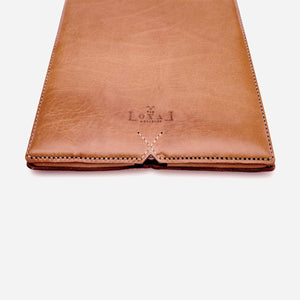 cropped image of a camel brown leather laptop sleeve with stitching and etched logo detailing.