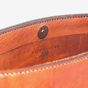Cropped image showing the inside of a caramel brown leather tote bag with stainless steel closure hardware and an etched makers mark.