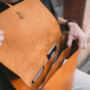 a person with a large caramel brown leather satchel sat on his lap, open with contents inside visible.