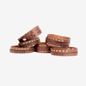 multiple stacks of dark brown leather wristbands with etched logo and type detailing as well as stitching details
